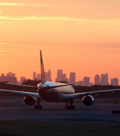 A plane taking off at JFK Airport during sunset with the NYC skyline in the background.